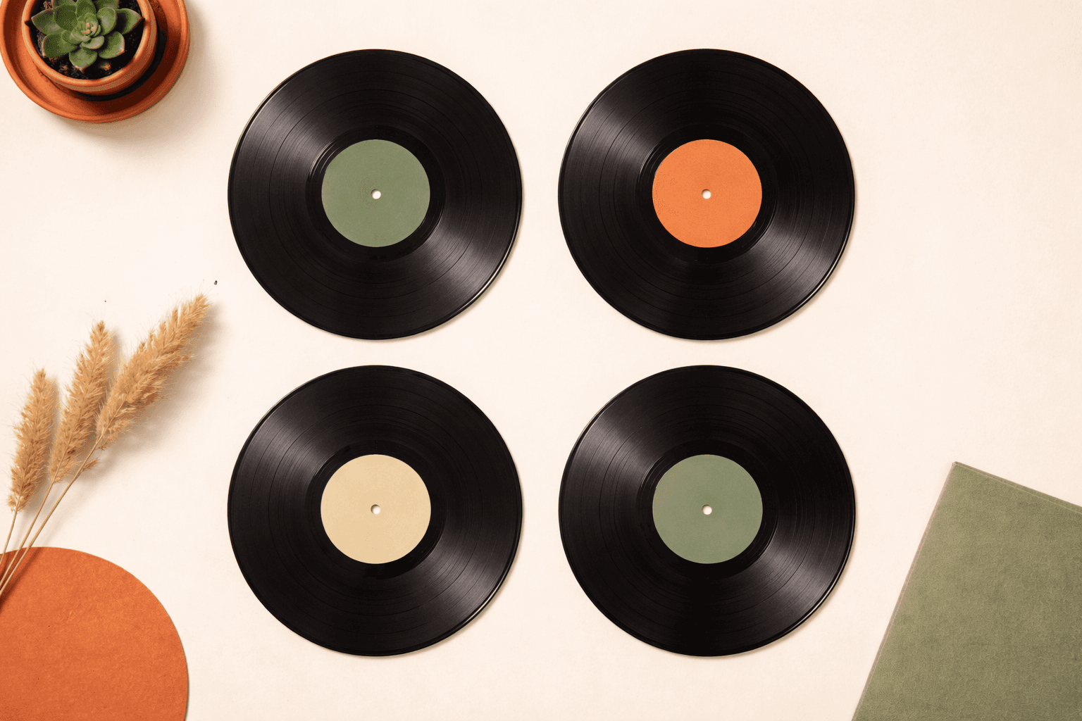 Four vinyl records arranged in a 2x2 grid with greenery accents on cream background